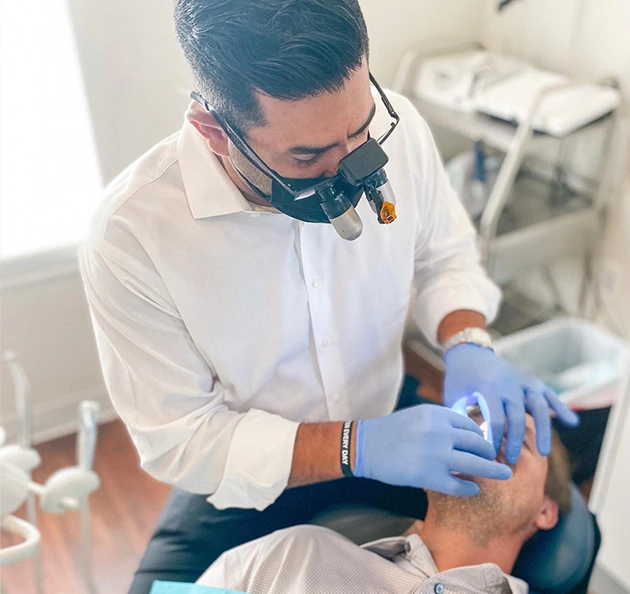 Dentist in white shirt using dental tools and gloves to examine a patient in a dental office, highlighting sedation dentistry and patient care at Warwick Dental.
