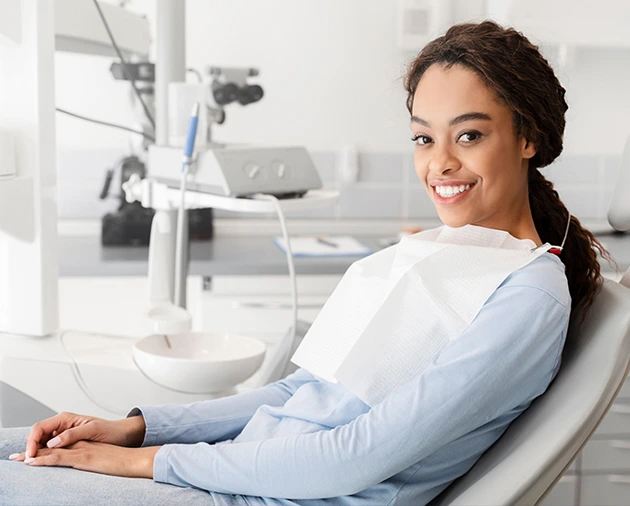 Smiling woman sitting in a dental chair, wearing a bib, in a modern dental office, reflecting comfort and care during a dental procedure.