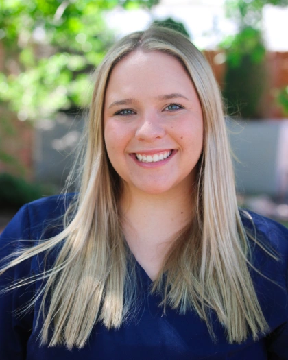 Abby Daniels, Implant Treatment Coordinator at Warwick Dental, smiling outdoors with long blonde hair and a navy shirt, embodying a welcoming demeanor in a friendly environment.