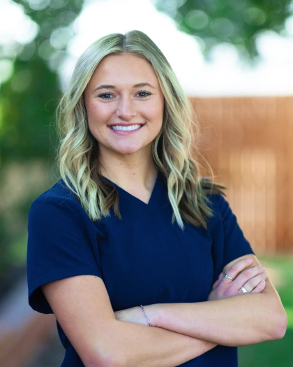 Abbyleigh Schilling, Dental Hygiene Assistant at Warwick Dental, smiling confidently in a navy scrubs top, standing outdoors with a blurred background.