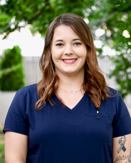 Bree Duncan, Lead Lab Technician and Dental Assistant at Warwick Dental, smiling in a navy scrub top, outdoor setting with greenery in the background.