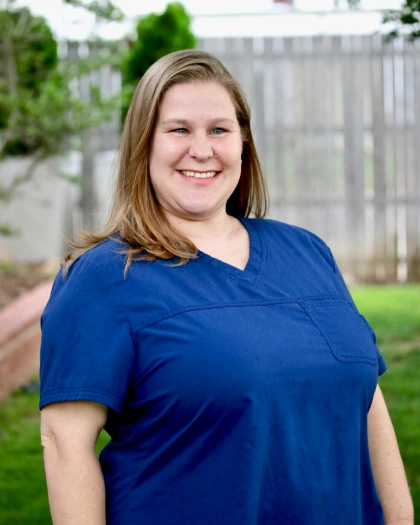 Candice Hoskins, Front Office Lead and Insurance Coordinator at Warwick Dental, smiling in blue scrubs against a green outdoor background.