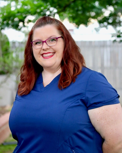 Kiela Rowan, Front Office and Dental Hygiene Coordinator at Warwick Dental, smiling outdoors in a blue scrub top, showcasing her role in promoting preventive care.