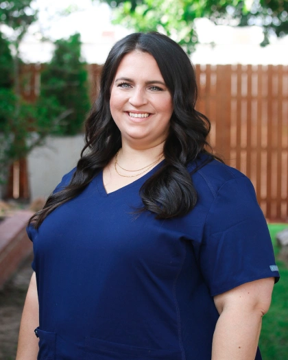 Kirsten Hollingshed, Operations Manager at Warwick Dental, smiling in a navy scrub top, standing outdoors with a wooden fence in the background.