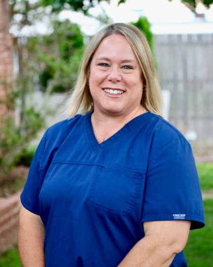 Laurie Love, Executive Manager at Warwick Dental, smiling in a blue scrub top, standing outdoors with greenery in the background.