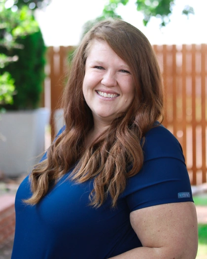 Lindsay Alvarez, smiling dental assistant at Warwick Dental, wearing a blue shirt, with a blurred outdoor background.