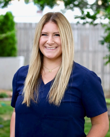 Maddie Davis, Dental Implant Liaison and Assistant at Warwick Dental, smiling outdoors in a navy scrubs top, showcasing her role in patient care and support.