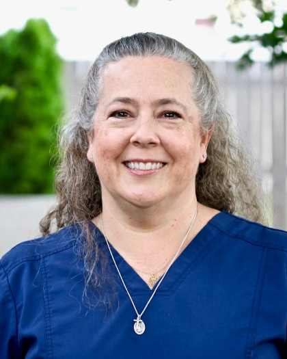 Teresa Larson, Lead Registered Dental Hygienist at Warwick Dental, smiling in a blue scrubs top with a natural background.