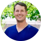 Smiling dental professional in a blue scrubs top, outdoors with greenery in the background, representing Warwick Dental's patient-centered care approach.