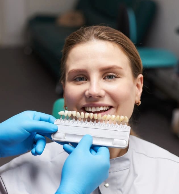 Woman smiling while a dental professional holds a shade guide for matching dental veneers at Warwick Dental, showcasing cosmetic dentistry services.