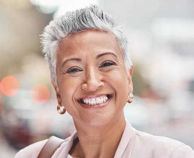 Smiling woman with short gray hair showcasing a confident smile, reflecting successful dental restoration and the benefits of dental implants.